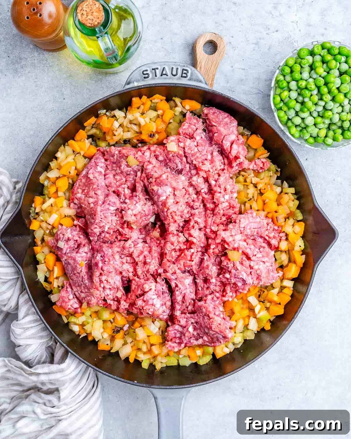 Homestyle Beef Shepherd's Delight 5 Raw ground beef over cooked veggies in a black skillet.