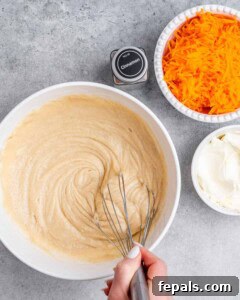 Effortless Carrot Cake 13 A whisk stirring cake batter in a white bowl.