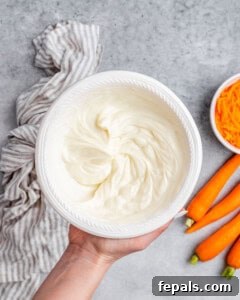 Effortless Carrot Cake 14 A hand holding whipped frosting in a bowl.