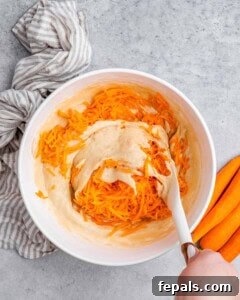 Effortless Carrot Cake 15 A spatula stirring in carrots to cake batter.