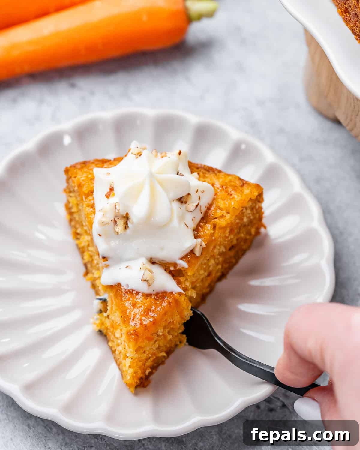 Effortless Carrot Cake 3 A fork taking a piece out of a slice of carrot cake, topped with creamy cheese frosting.