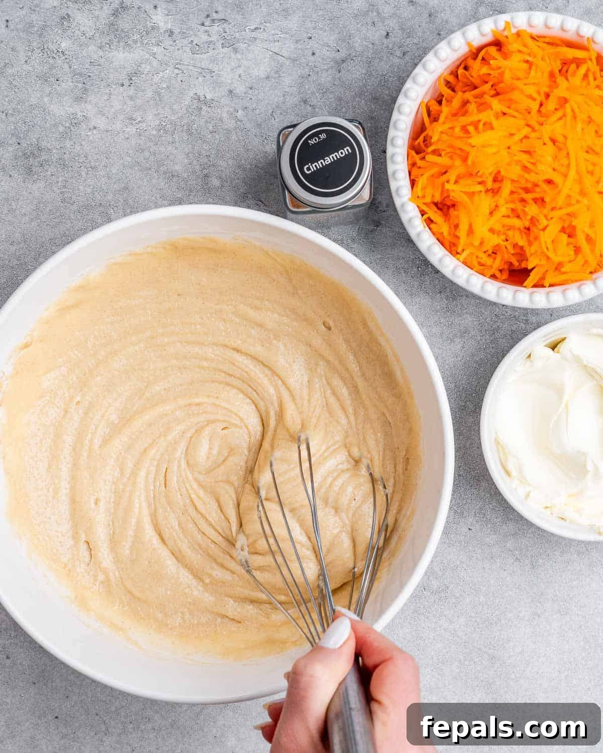 Effortless Carrot Cake 5 A whisk stirring cake batter in a white bowl.
