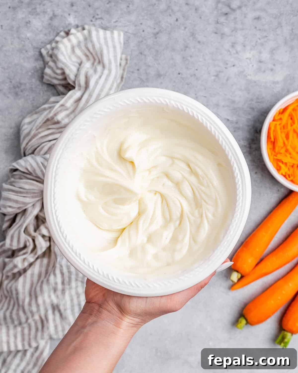 Effortless Carrot Cake 7 A hand holding whipped frosting in a bowl.