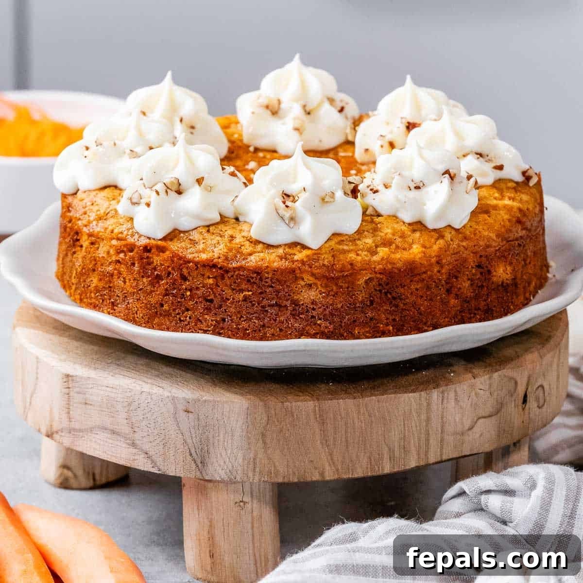 Effortless Carrot Cake 10 A round carrot cake with slice cut off topped with creamy cheese frosting, garnished with edible flowers.