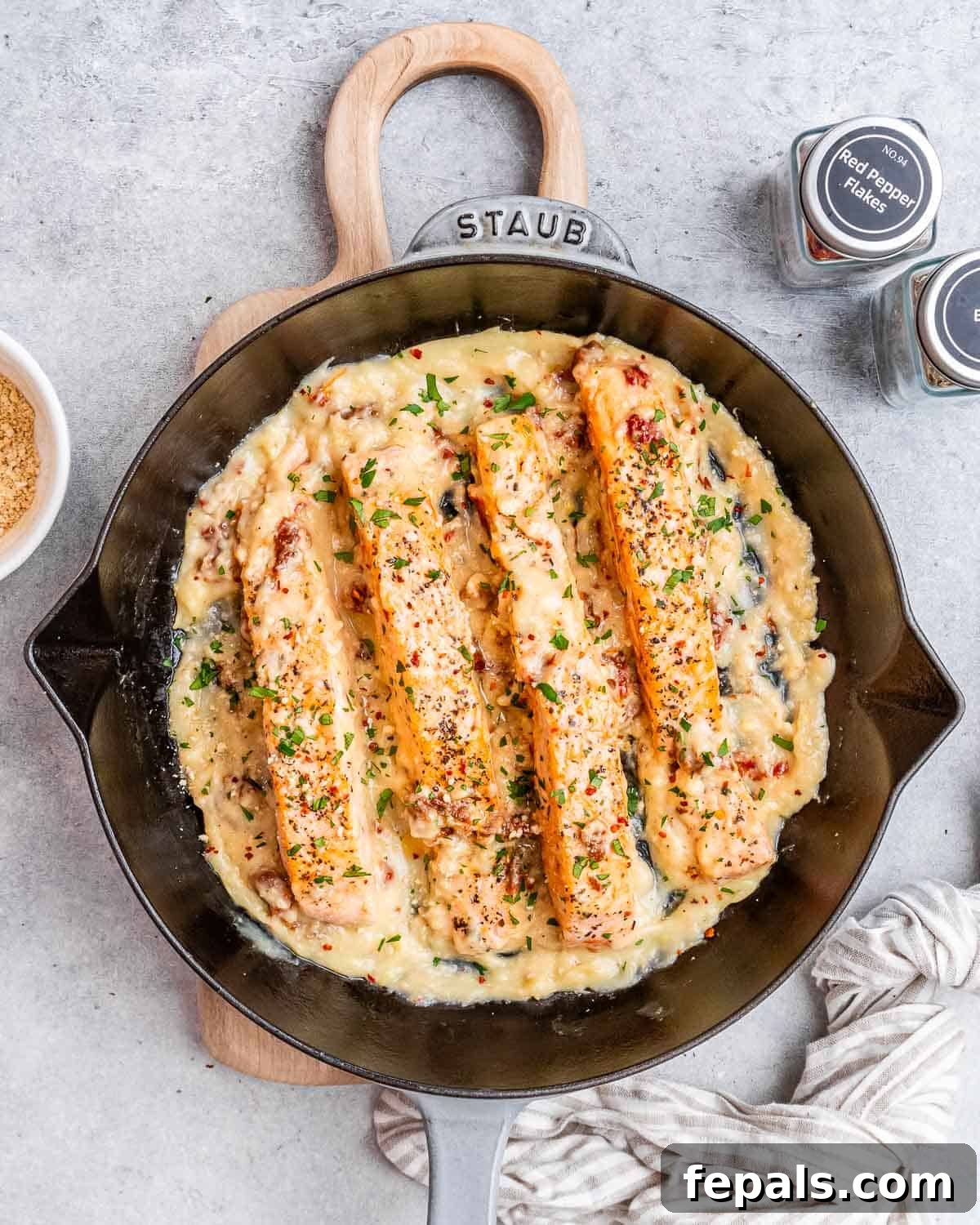 Proposal Salmon 2 A black skillet with four salmon fillets nestled in a vibrant creamy sauce, garnished with fresh herbs.
