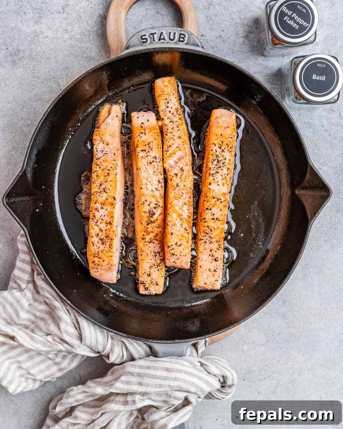 Proposal Salmon 5 Four perfectly seared salmon fillets resting in a black skillet.