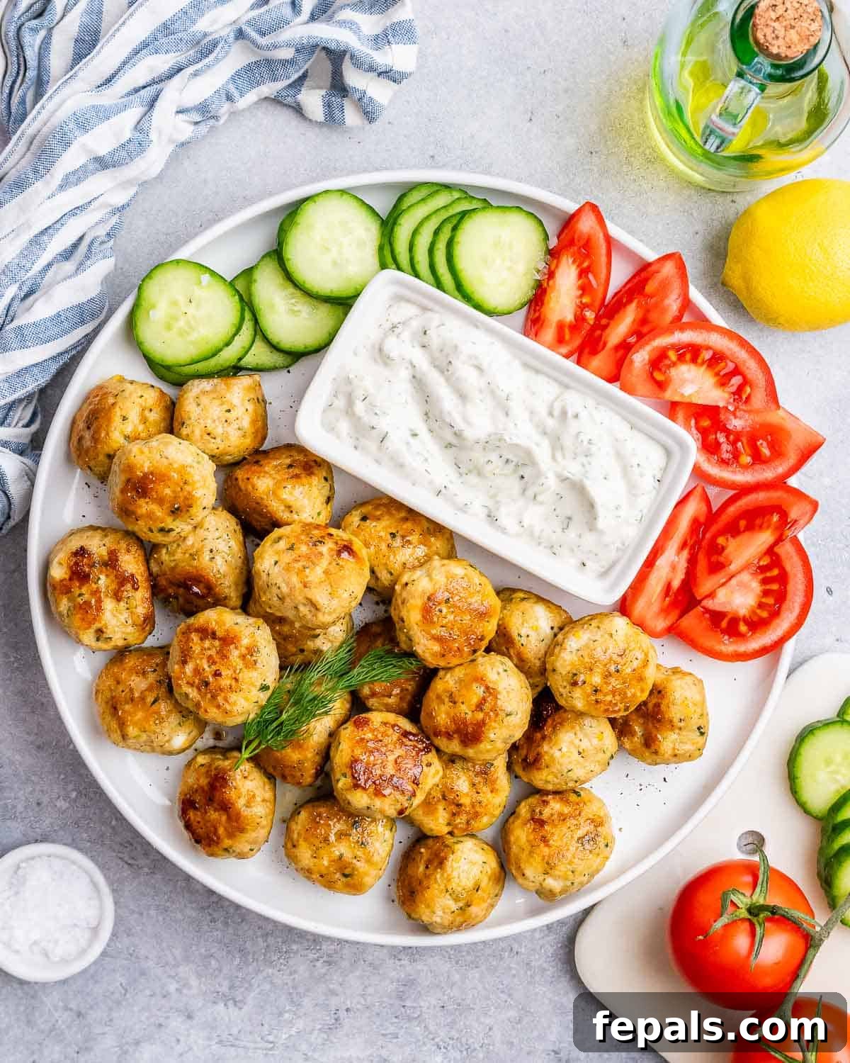 Flavorful Greek Turkey Meatballs served on a plate with fresh cucumber and tomato salad, alongside a bowl of creamy tzatziki sauce for dipping.