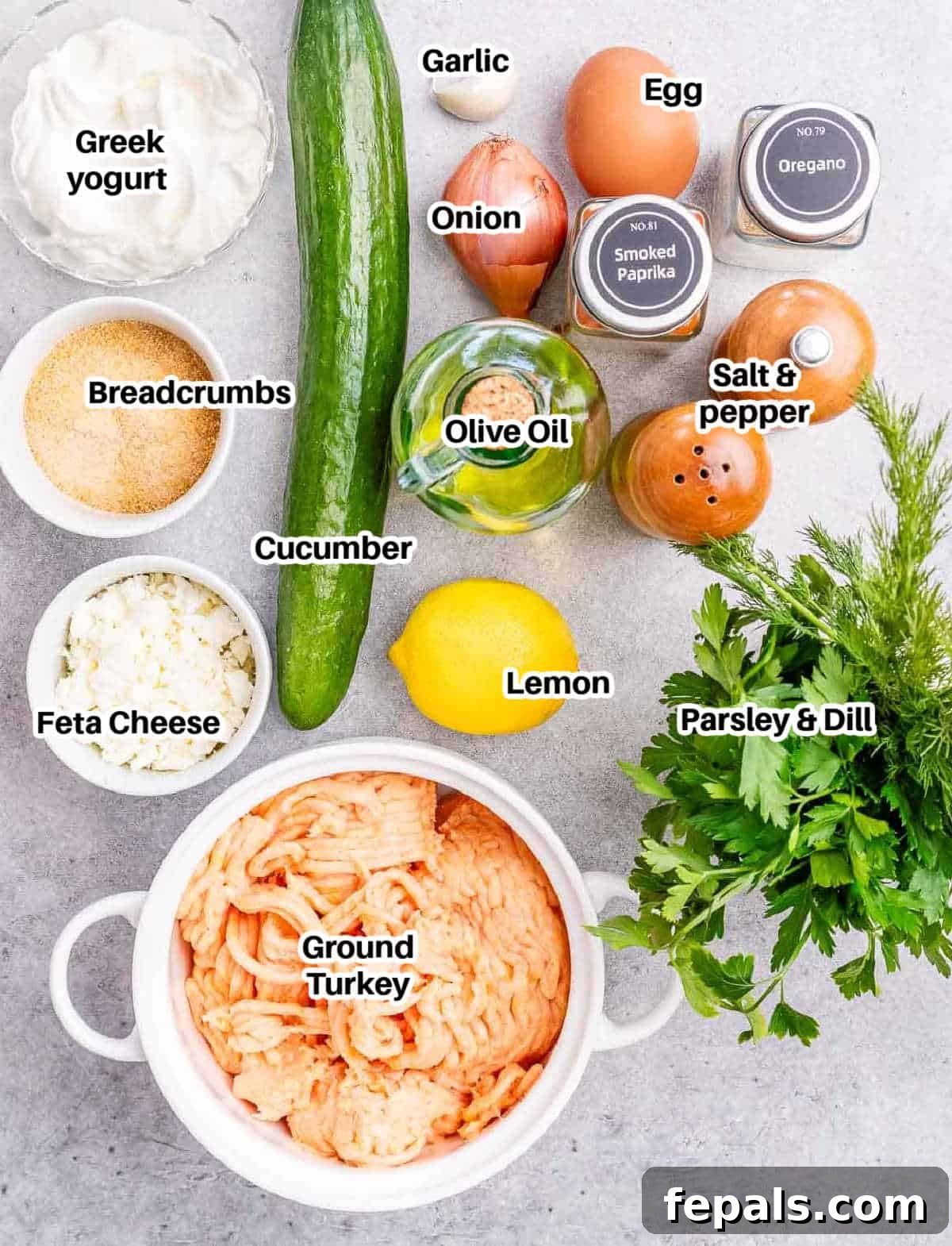 A collection of fresh ingredients laid out on a white surface, including ground turkey, feta cheese, herbs, eggs, and breadcrumbs, ready for making Greek meatballs.