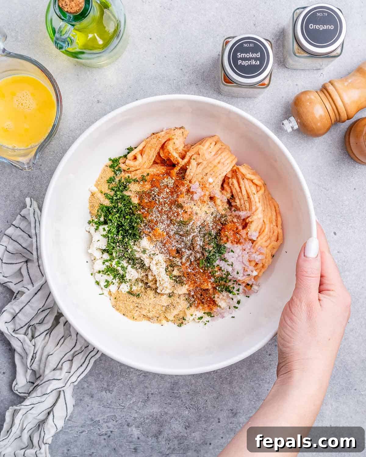A large white mixing bowl containing lean ground turkey, crumbled feta cheese, and finely chopped fresh herbs and shallots, ready to be combined for the Greek meatballs.