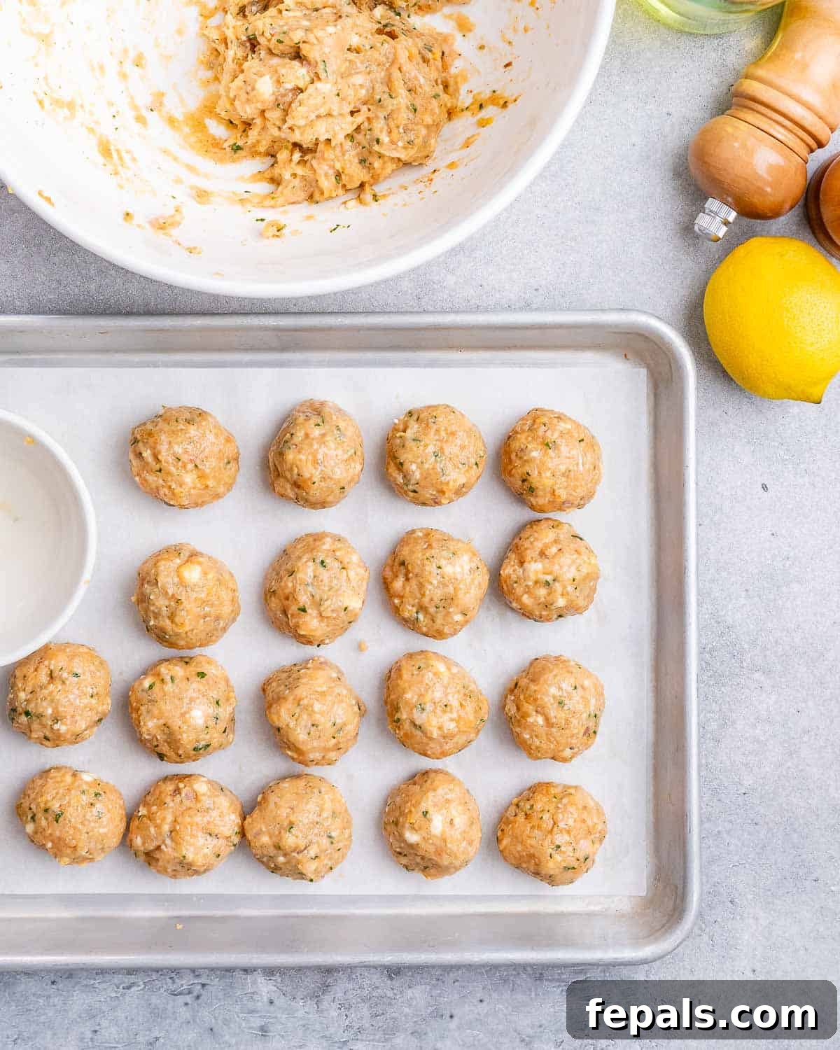 Uniformly shaped raw Greek turkey meatballs neatly arranged on a parchment-lined baking sheet, prepared for chilling before cooking.