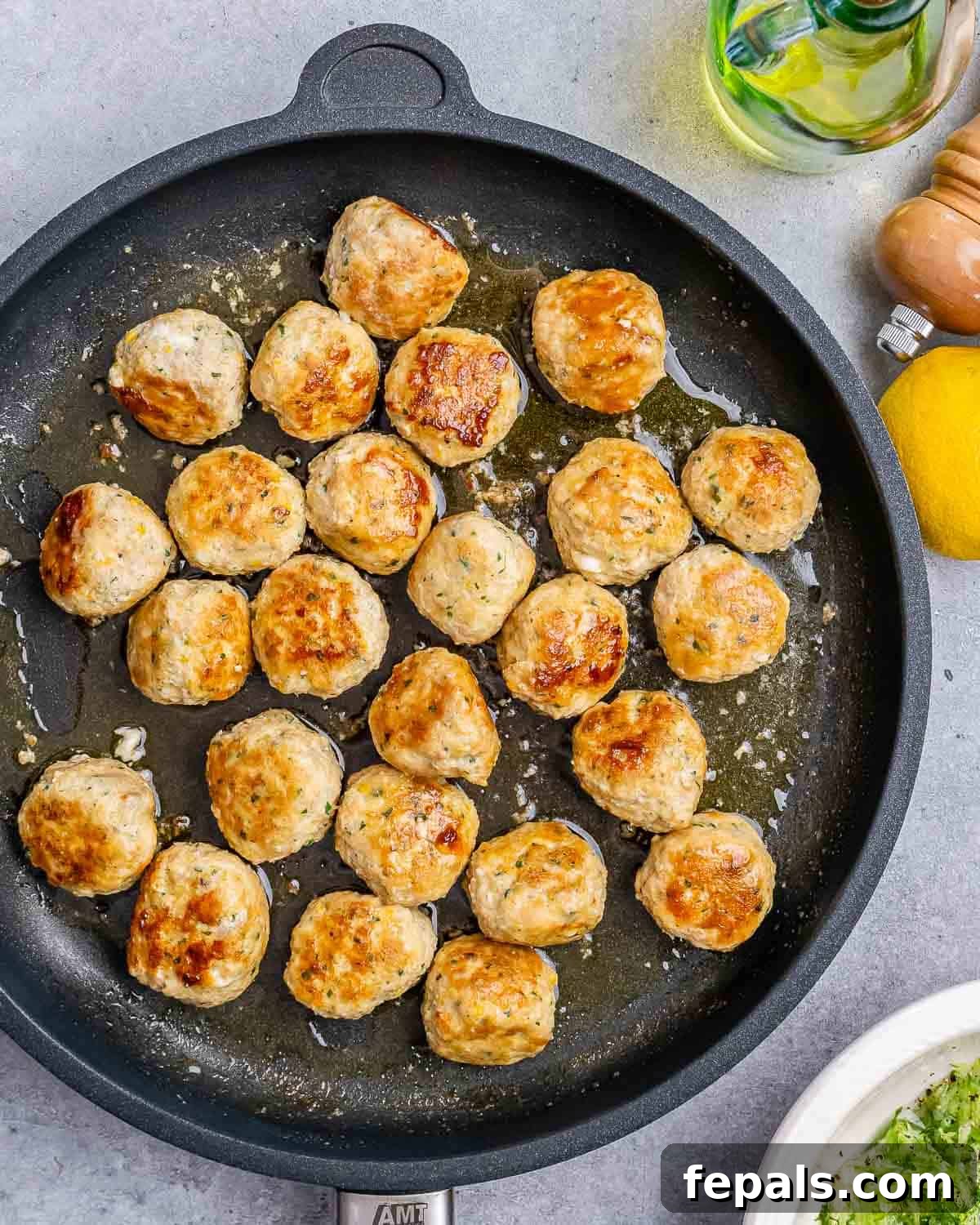 Cooked, golden-brown Greek turkey meatballs sizzling in a black cast iron skillet, indicating they are nearly ready to serve.