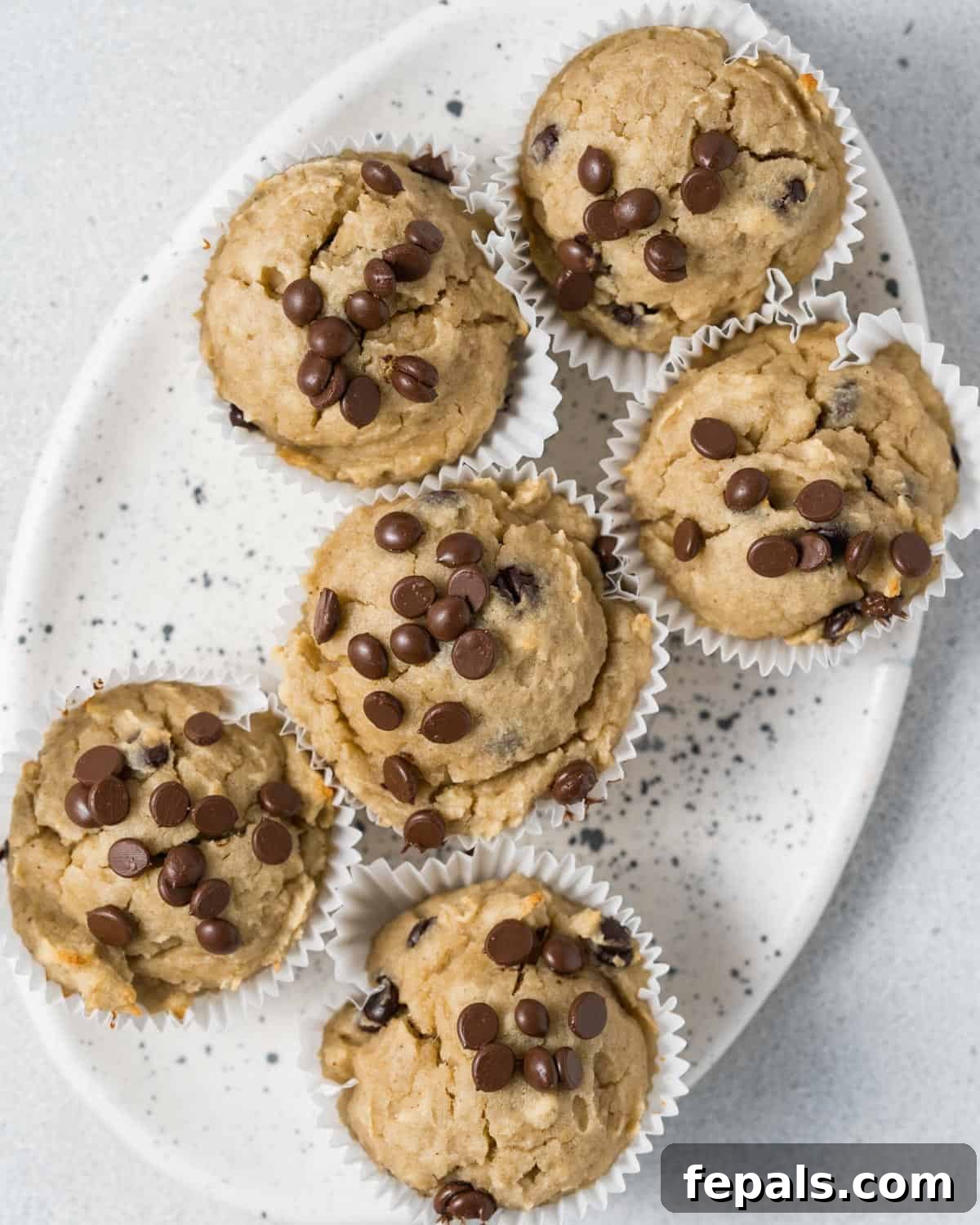 Six golden-brown almond flour banana muffins on a white plate, garnished with chocolate chips.