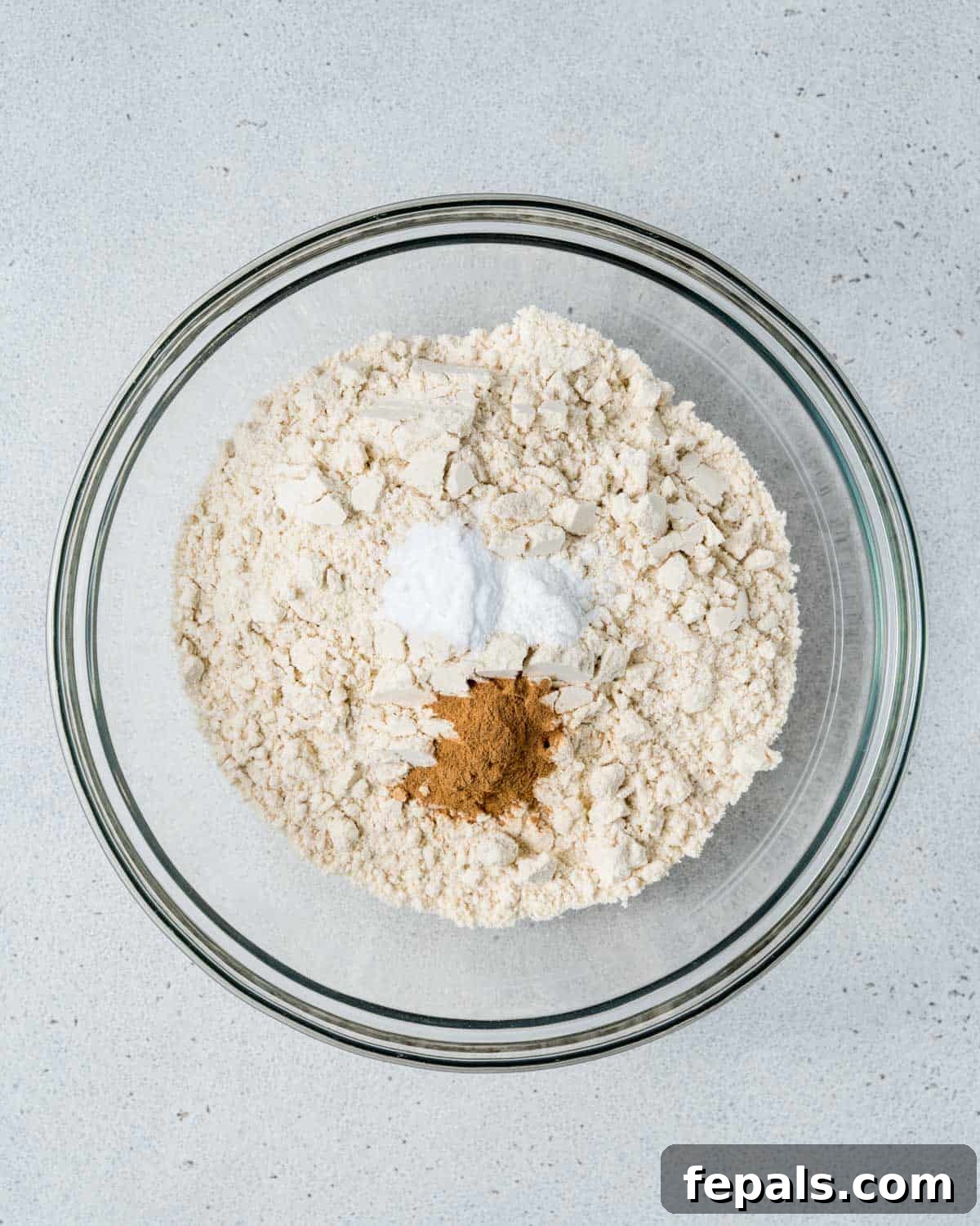Almond flour, baking soda, cinnamon, and baking powder are measured and mixed together in a separate bowl.