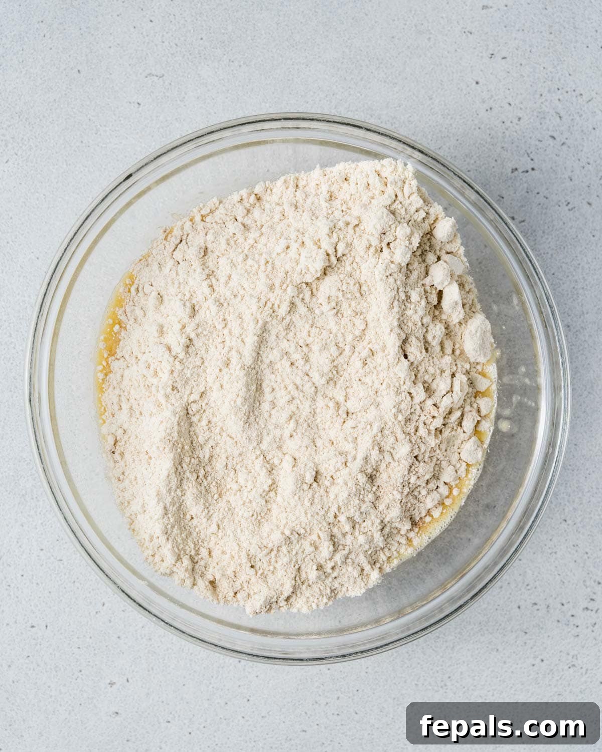 The dry almond flour mixture being carefully poured over the wet banana and egg mixture in a large bowl, ready for folding.