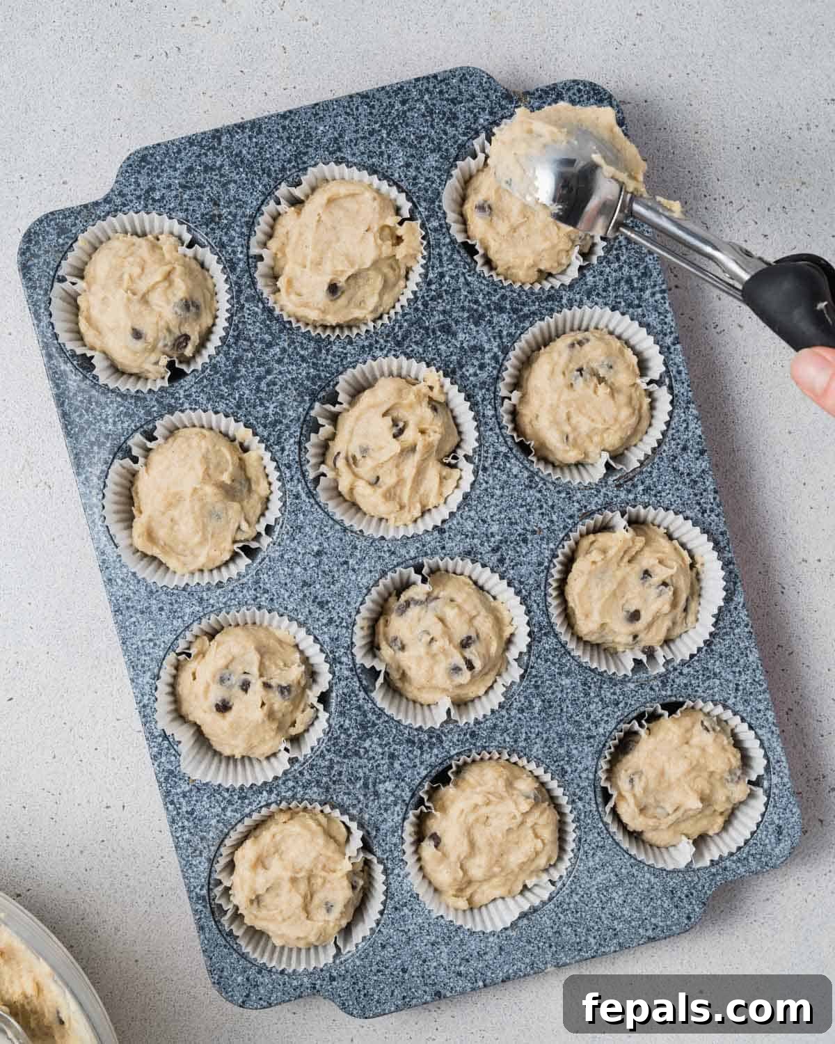 Muffin batter is scooped into prepared muffin liners in a baking pan, filling each cup evenly.