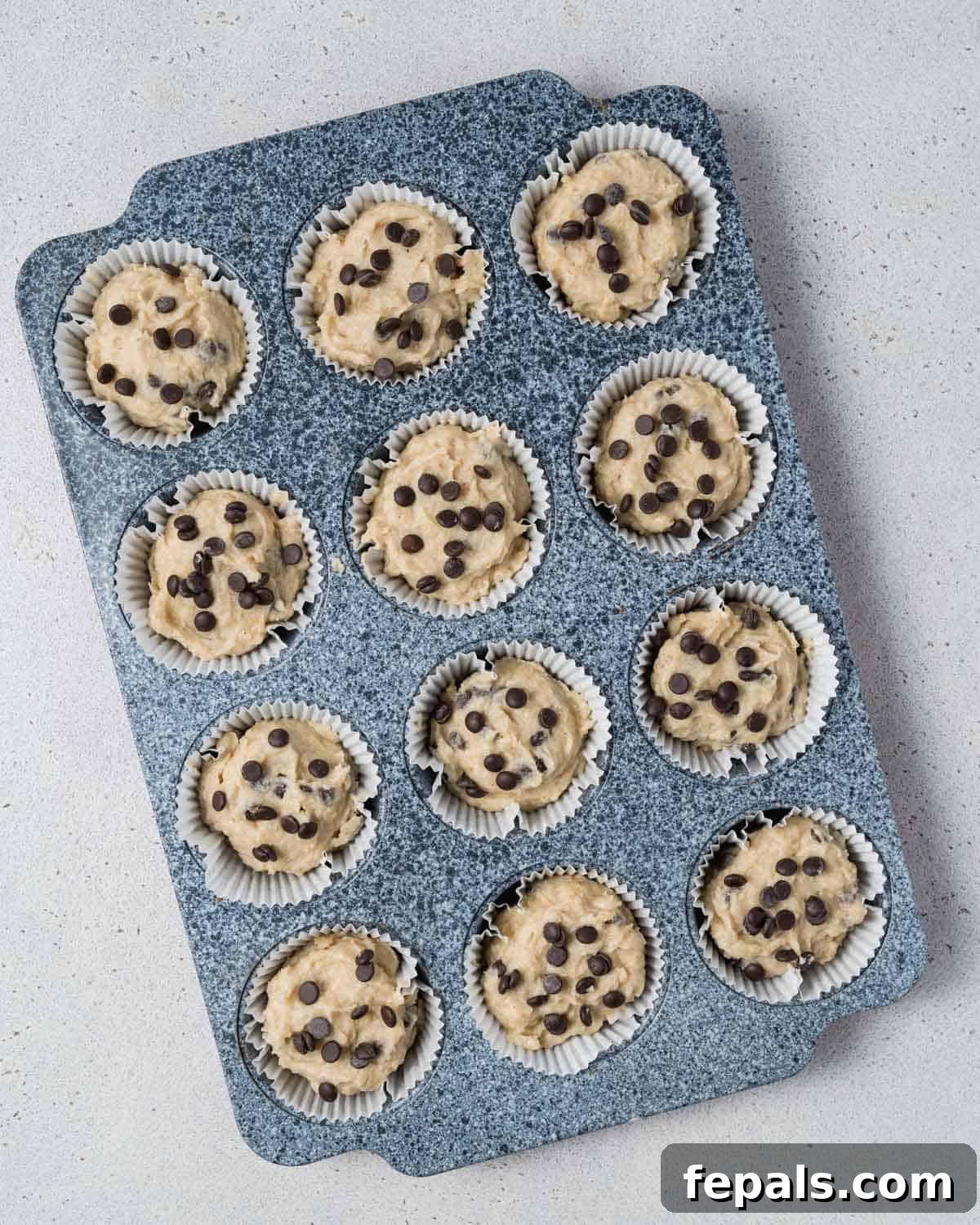 Muffin batter in a pan, topped generously with additional chocolate chips and chopped walnuts for extra flavor and texture.