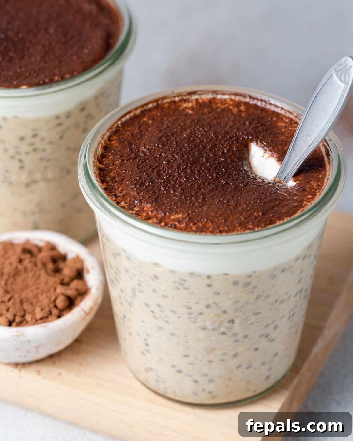 Creamy Tiramisu Overnight Oats 2 A jar of Tiramisu Overnight Oats, topped with a generous dusting of cocoa powder, with a spoon nestled inside.