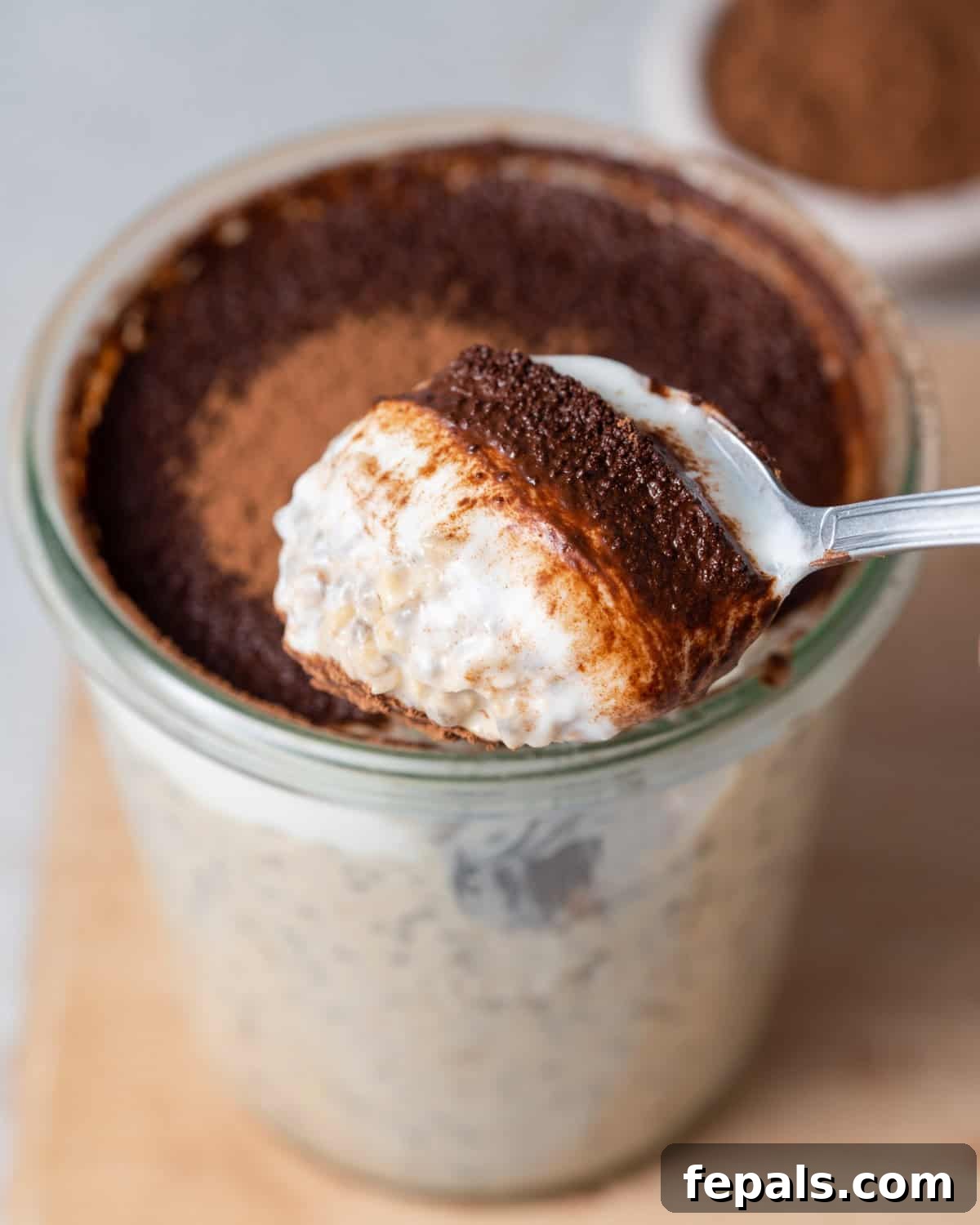 Creamy Tiramisu Overnight Oats 6 A beautifully assembled jar of Tiramisu Overnight Oats with a spoon, showing the creamy layers and cocoa dusting.