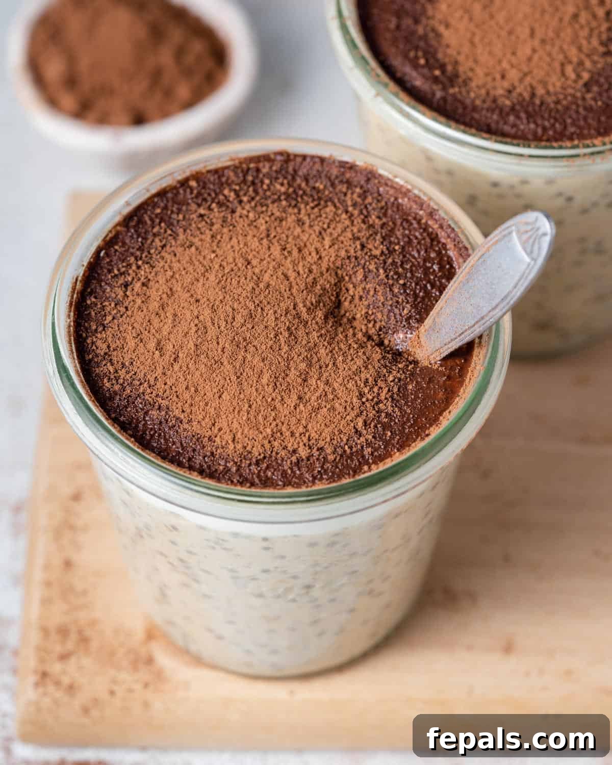 Creamy Tiramisu Overnight Oats 8 A spoon digging into creamy Tiramisu Overnight Oats, topped with cocoa powder, in a glass jar.