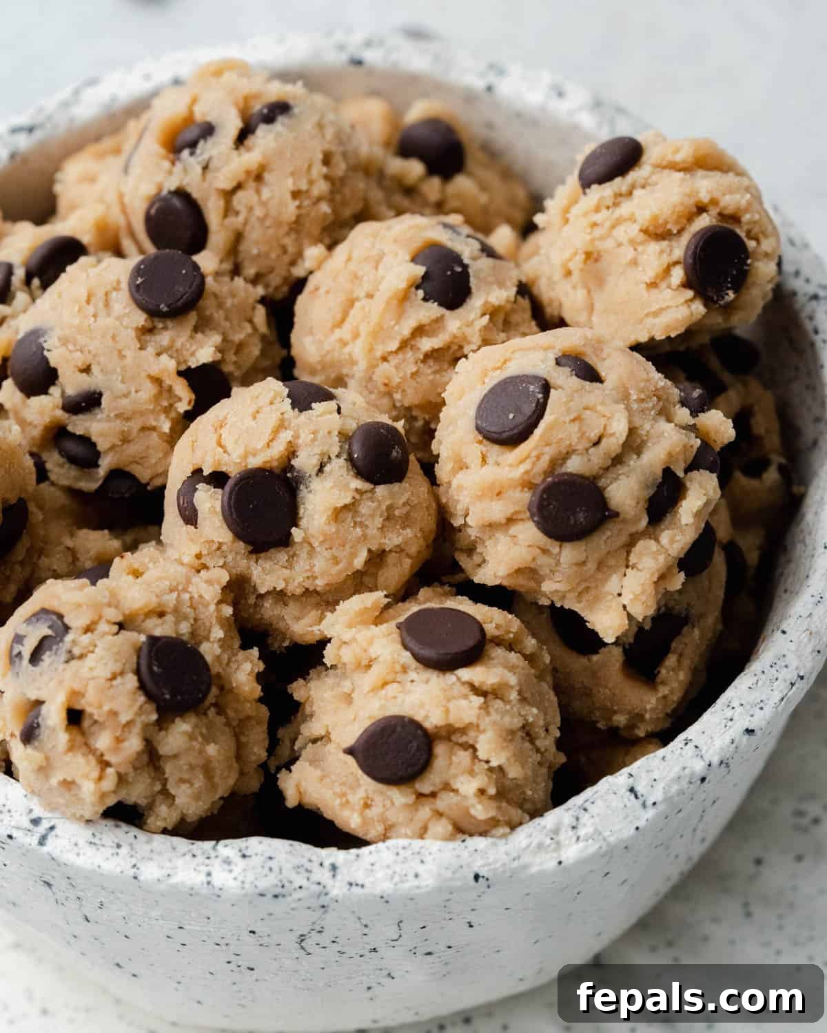 Guilt-Free Protein Cookie Dough 2 Delicious balls of edible protein cookie dough in a speckled white bowl, ready to be enjoyed.
