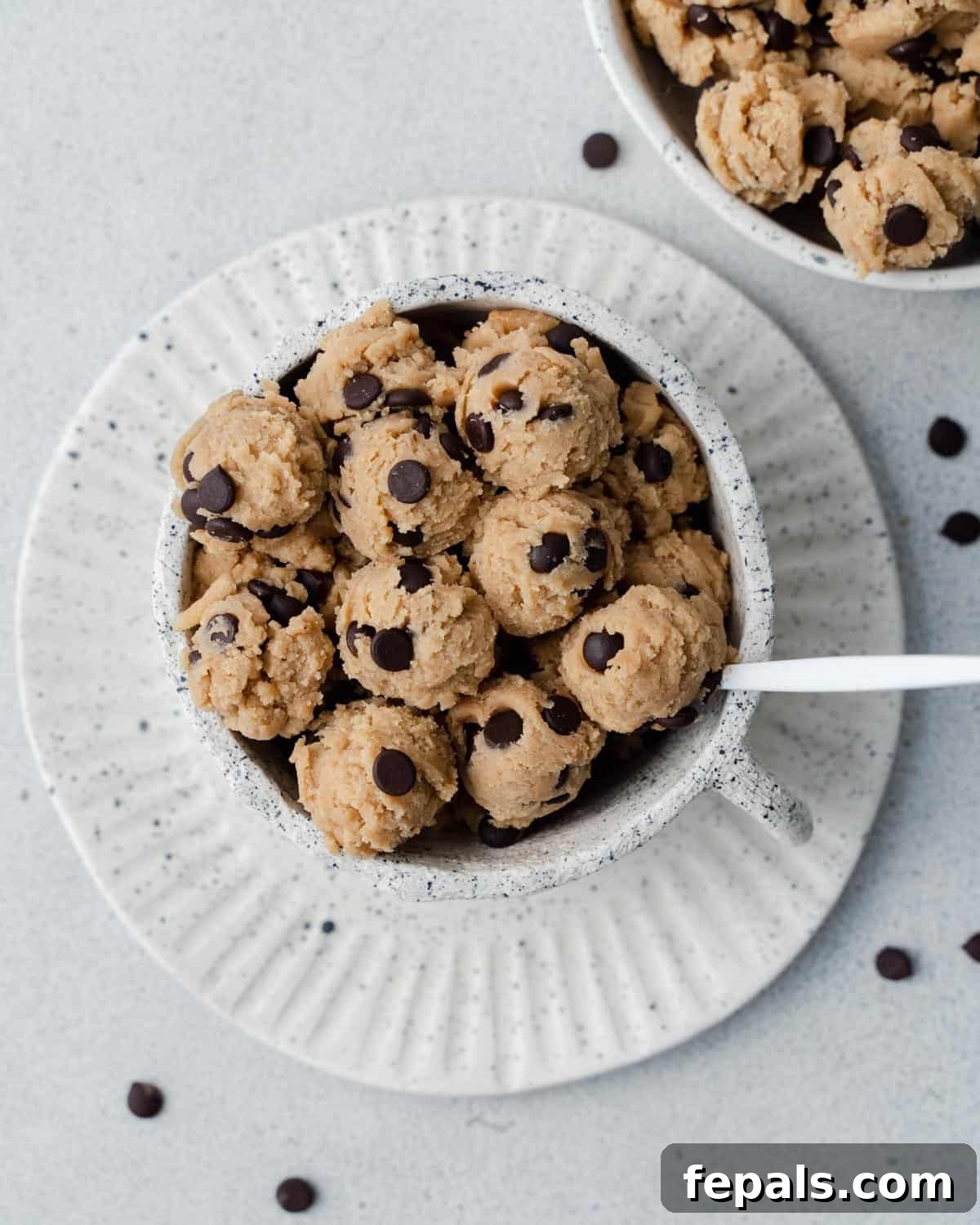 Guilt-Free Protein Cookie Dough 12 A bowl of edible chocolate chip cookie dough, garnished with extra chocolate chips, on a white plate.