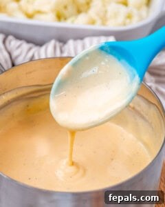 A blue spoon dripping cheese sauce into a pot of sauce.