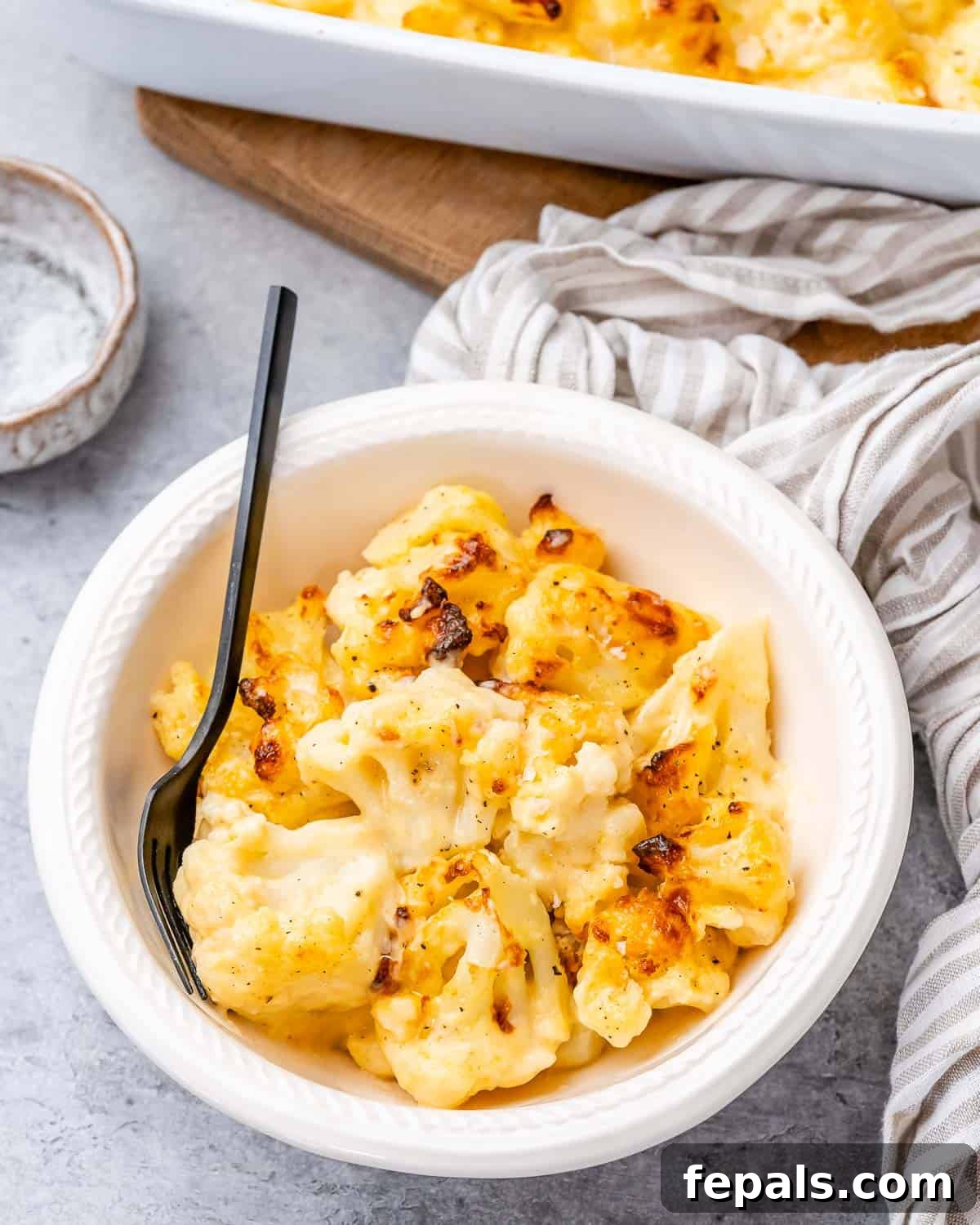 Cheesy cauliflower in a white bowl with a fork on the side.