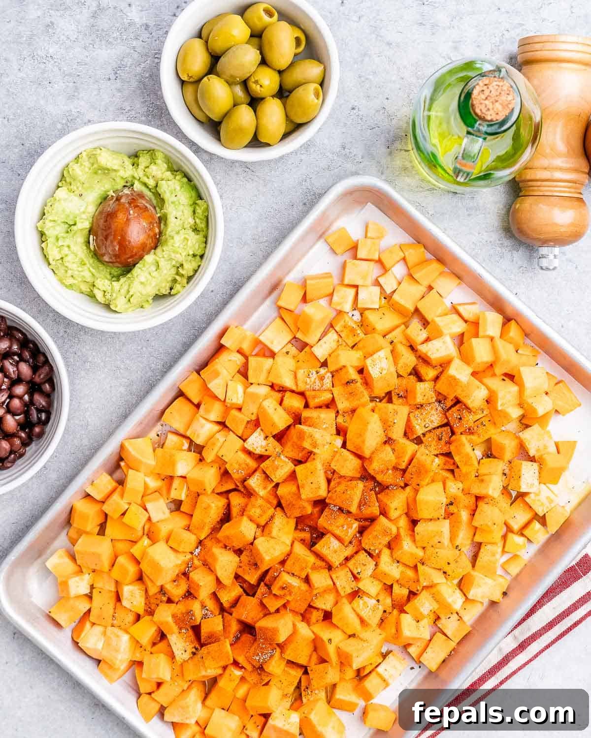 Diced sweet potatoes tossed with olive oil and seasoning, ready to be roasted on a parchment-lined baking sheet.