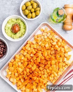 Diced sweet potatoes tossed with olive oil and seasoning, ready to be roasted, on a sheet pan next to other taco ingredients.