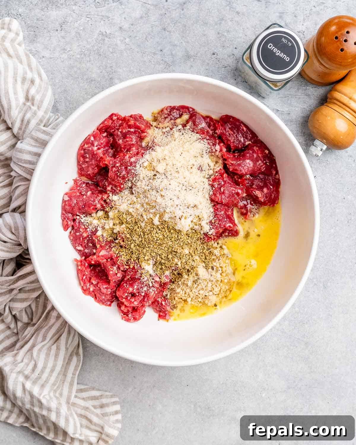 Golden Air Fryer Meatballs 4 All the raw ingredients for the meatballs, including ground beef, almond flour, and spices, are combined in a large white mixing bowl on a kitchen counter.