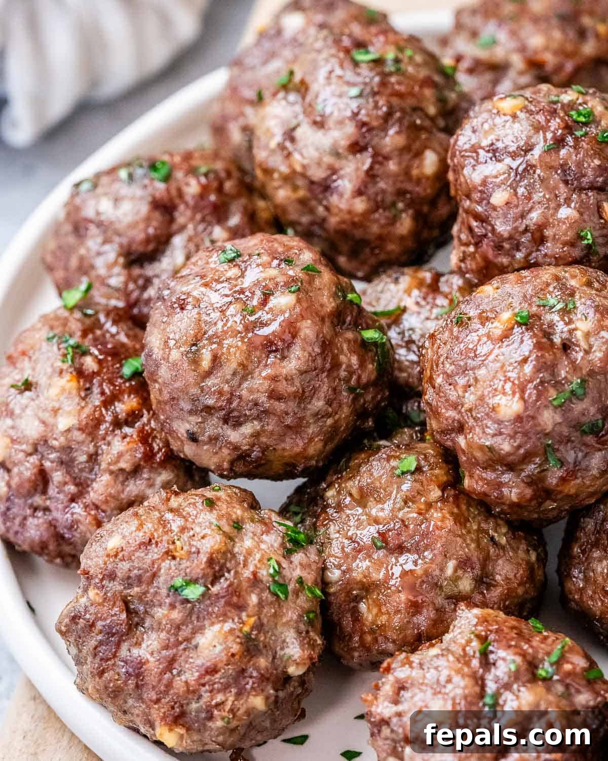 Golden Air Fryer Meatballs 8 A beautifully composed shot of cooked air fryer meatballs served on a white round plate, placed on a wooden cutting board, ready to be enjoyed.