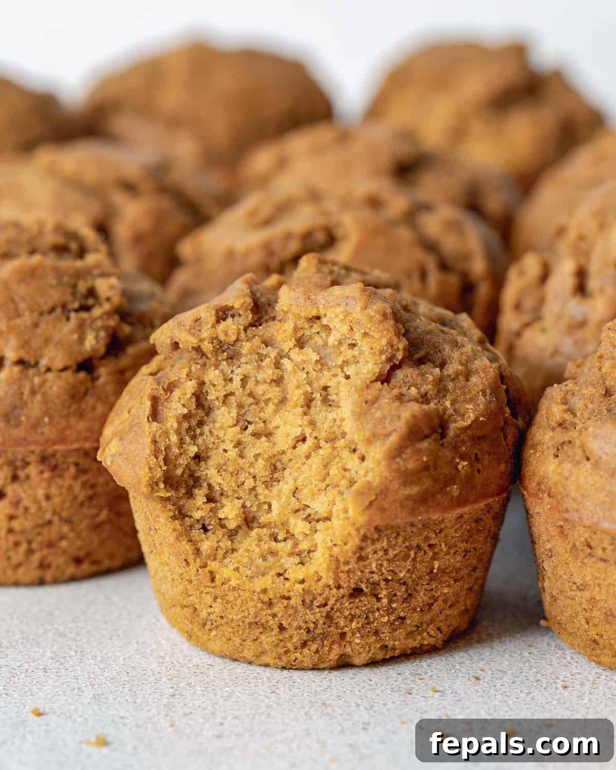 A perfectly baked pumpkin banana muffin with a bite taken out, revealing its moist, tender, and spiced interior. It sits on a white plate, inviting a second bite.