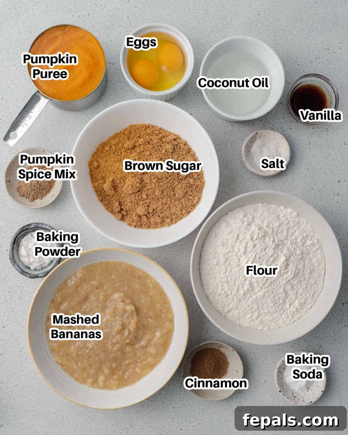 A flat lay of ingredients for pumpkin banana muffins, including mashed bananas, canned pumpkin puree, eggs, brown sugar, flour, and a selection of warming spices, neatly arranged on a white backdrop.