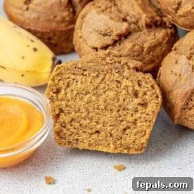 a sliced pumpkin muffin by a bowl of pumpkin sauce and other muffins. The muffin reveals its moist, spiced interior, perfectly complemented by the other autumnal elements.