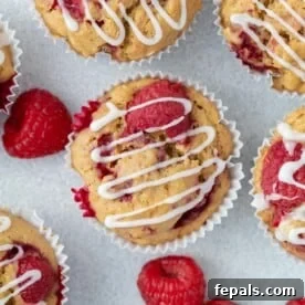 raspberry muffins on a flat surface topped with a drizzle if icing sugar.