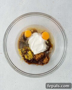 Wet ingredients (egg, yogurt, sugar, oil, lemon) are added to a bowl, ready to be whisked.