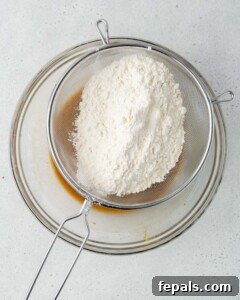 Flour being gently poured over the wet egg mixture in a bowl.