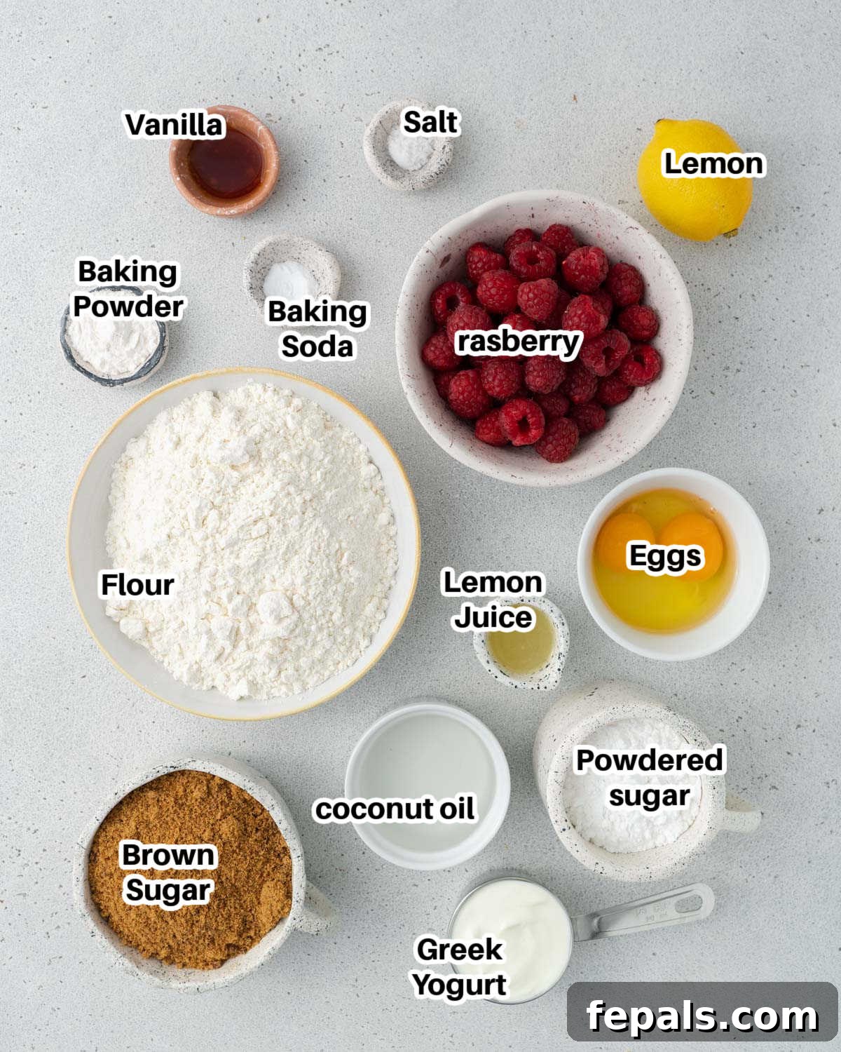 A flat lay photograph of all the fresh and dry ingredients required to make raspberry muffins, neatly arranged on a kitchen counter.
