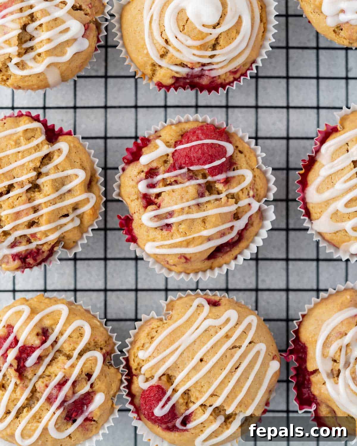 Freshly baked raspberry muffins cooling on a wire rack, waiting to be glazed.