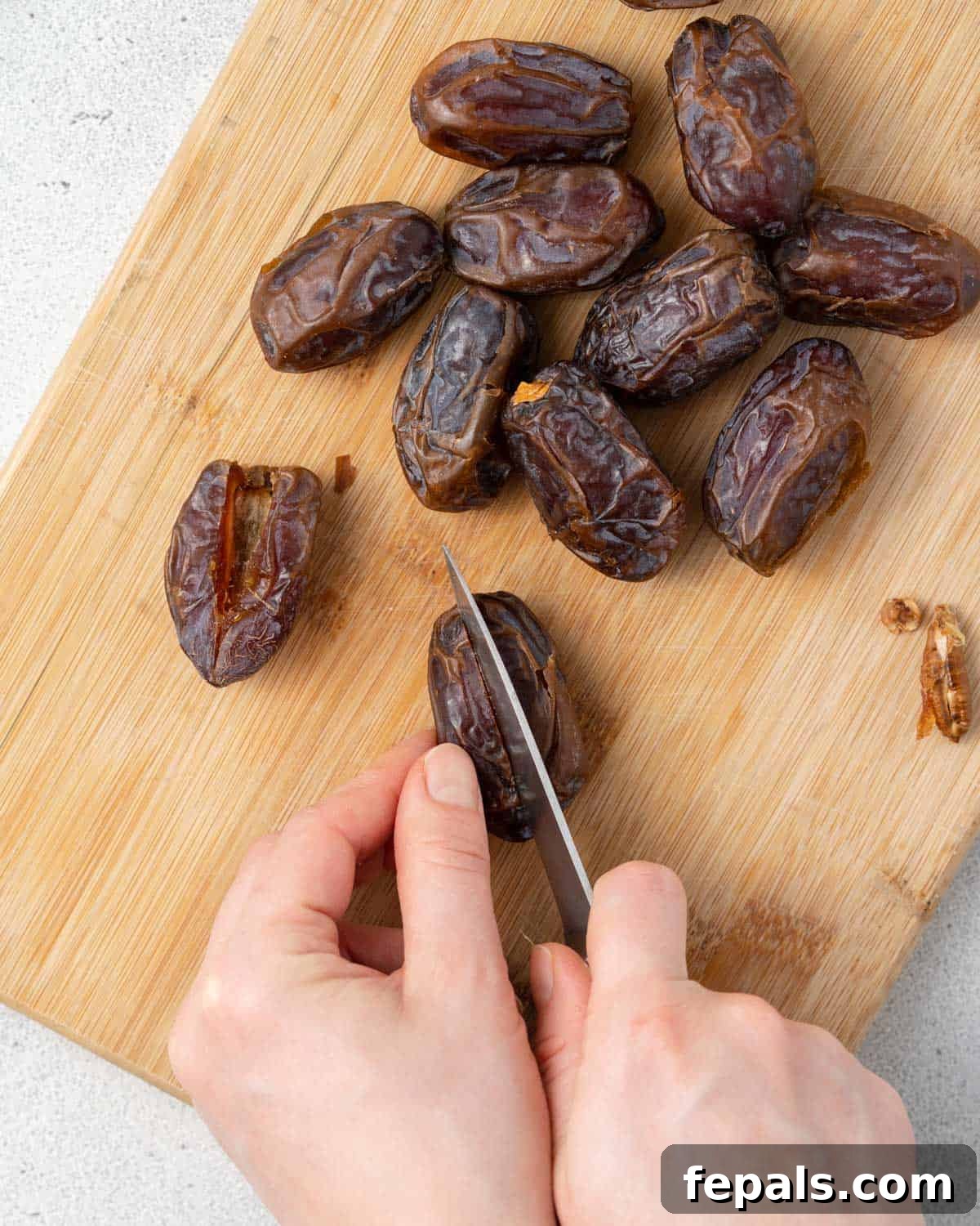 A hand with a knife slicing open a date to remove the pit.