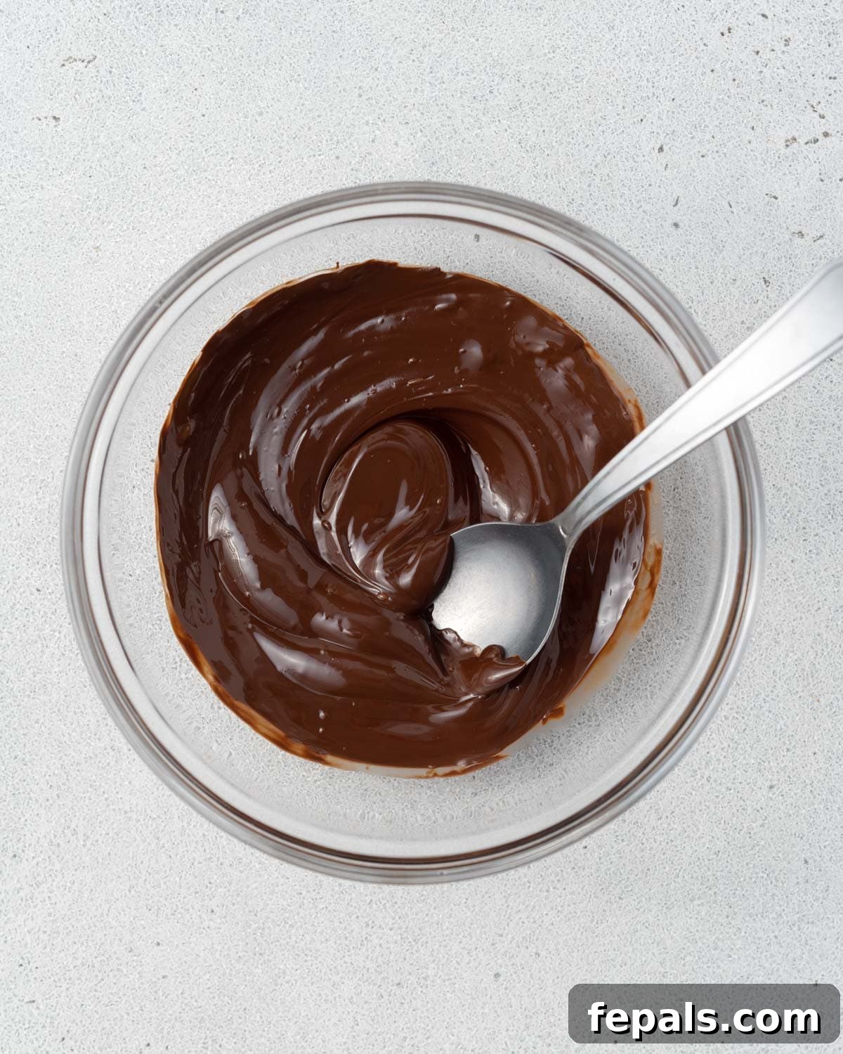 A bowl of melted dark chocolate with a spoon.