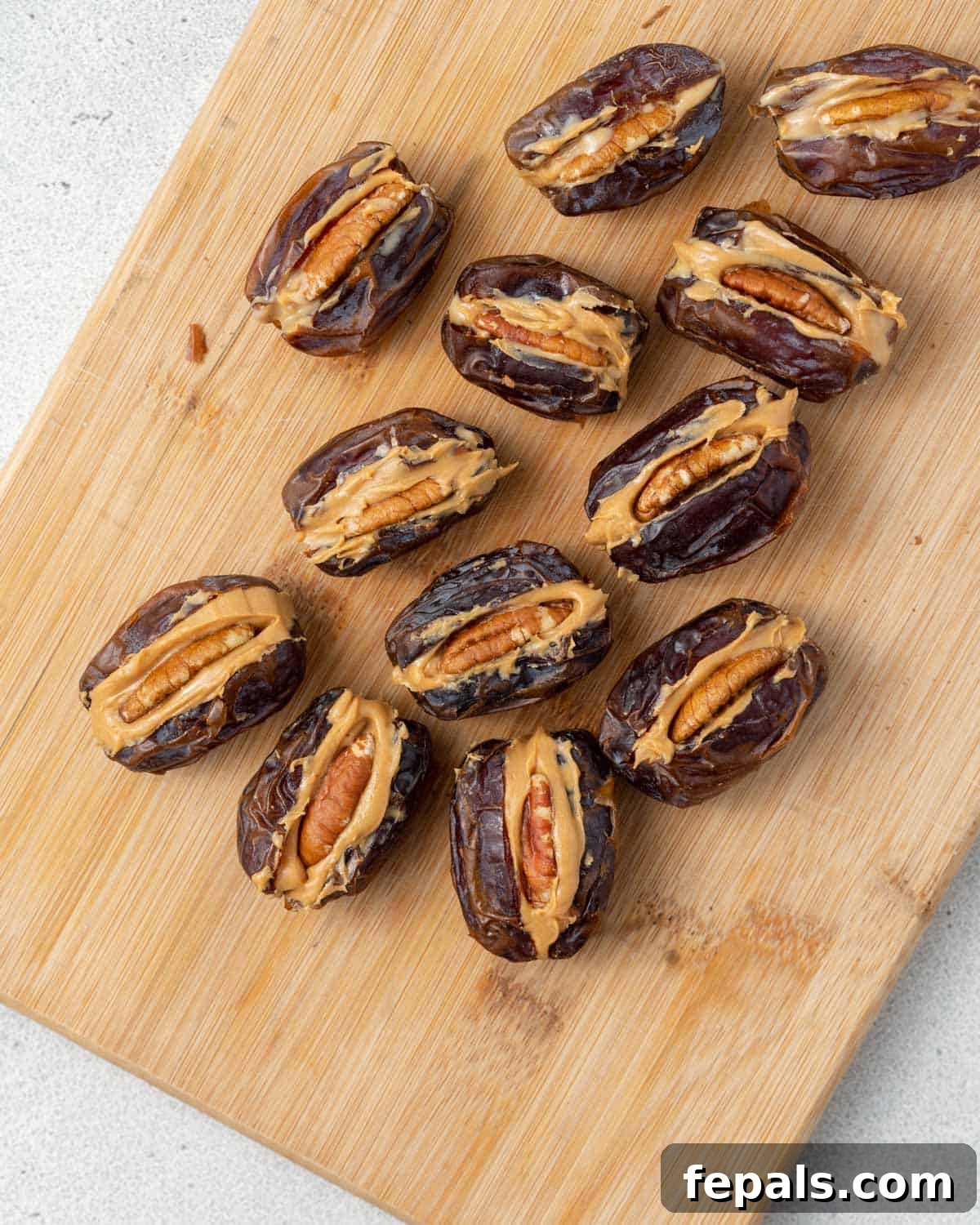 A cutting board with stuffed dates arranged before dipping, filled with peanut butter and pecans