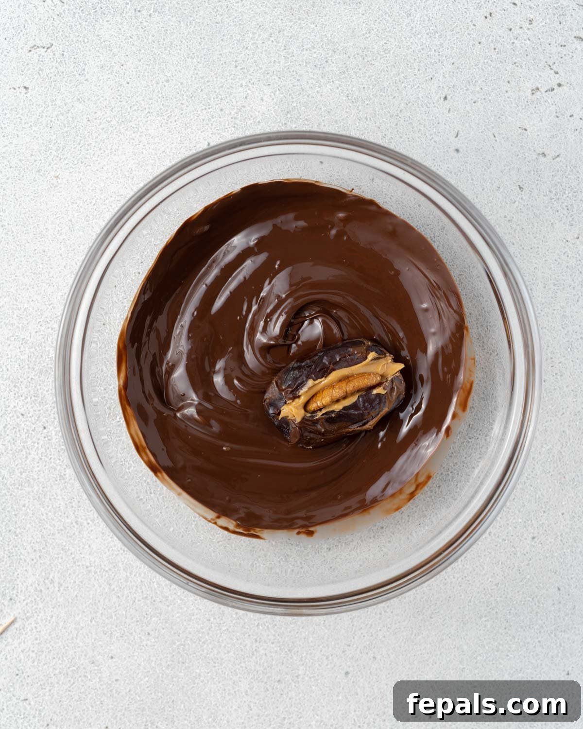 A single date being dipped in the bowl of melted chocolate