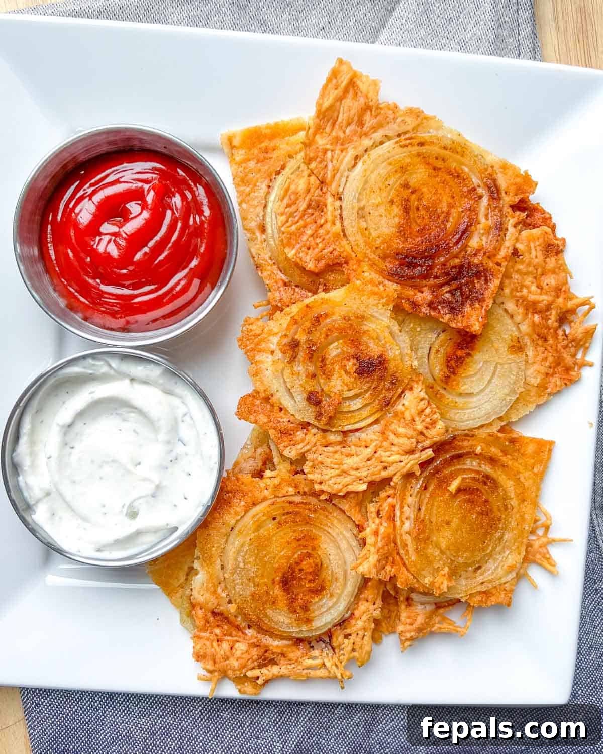 Golden Crunch Onion Rings 2 Crispy low-carb onion ring chips served on a plate with two small bowls of dipping sauces: creamy tzatziki and classic ketchup.