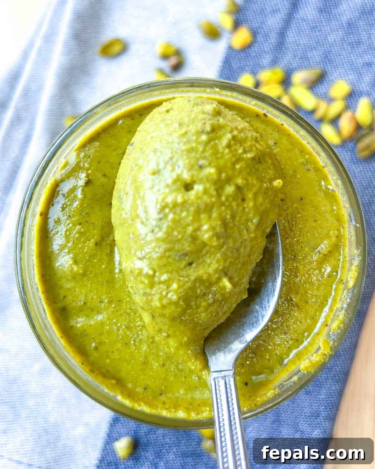 Decadent Pistachio Cream 12 A spoon scooping up a generous portion of creamy homemade pistachio cream from a jar.