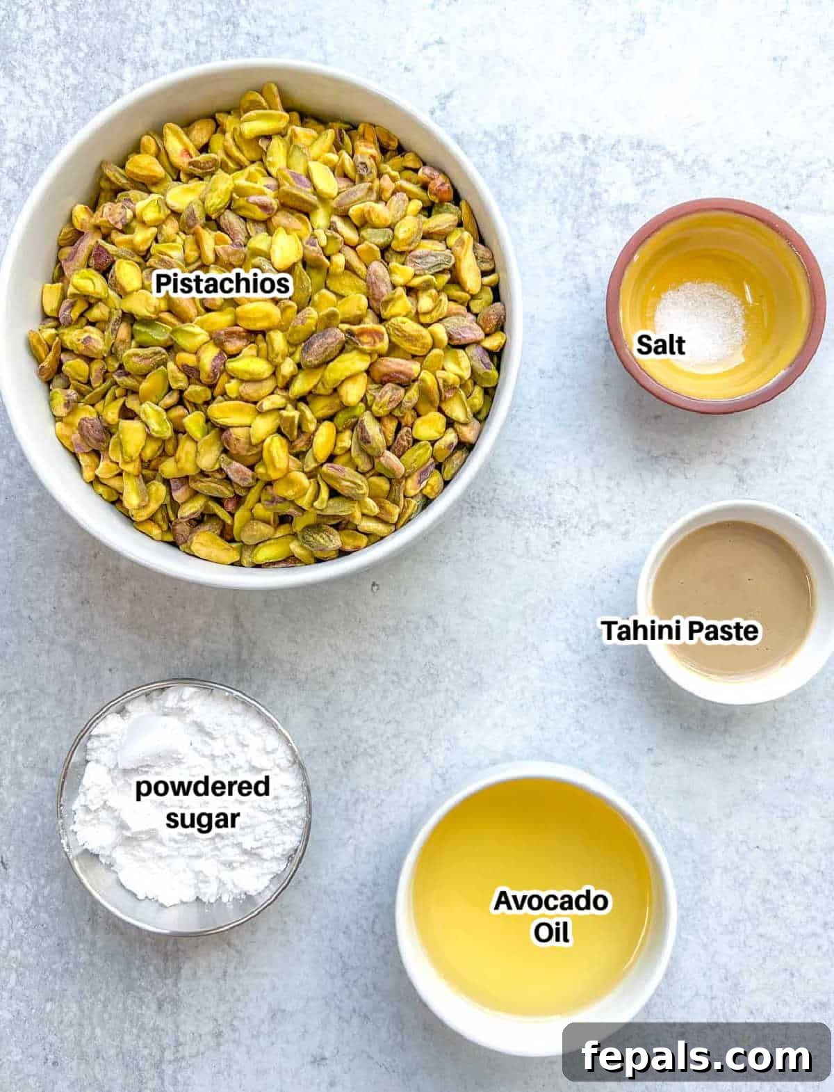 Decadent Pistachio Cream 3 A flat lay photograph showcasing all the ingredients needed to make homemade pistachio cream: raw pistachios, powdered sugar, avocado oil, and tahini paste.