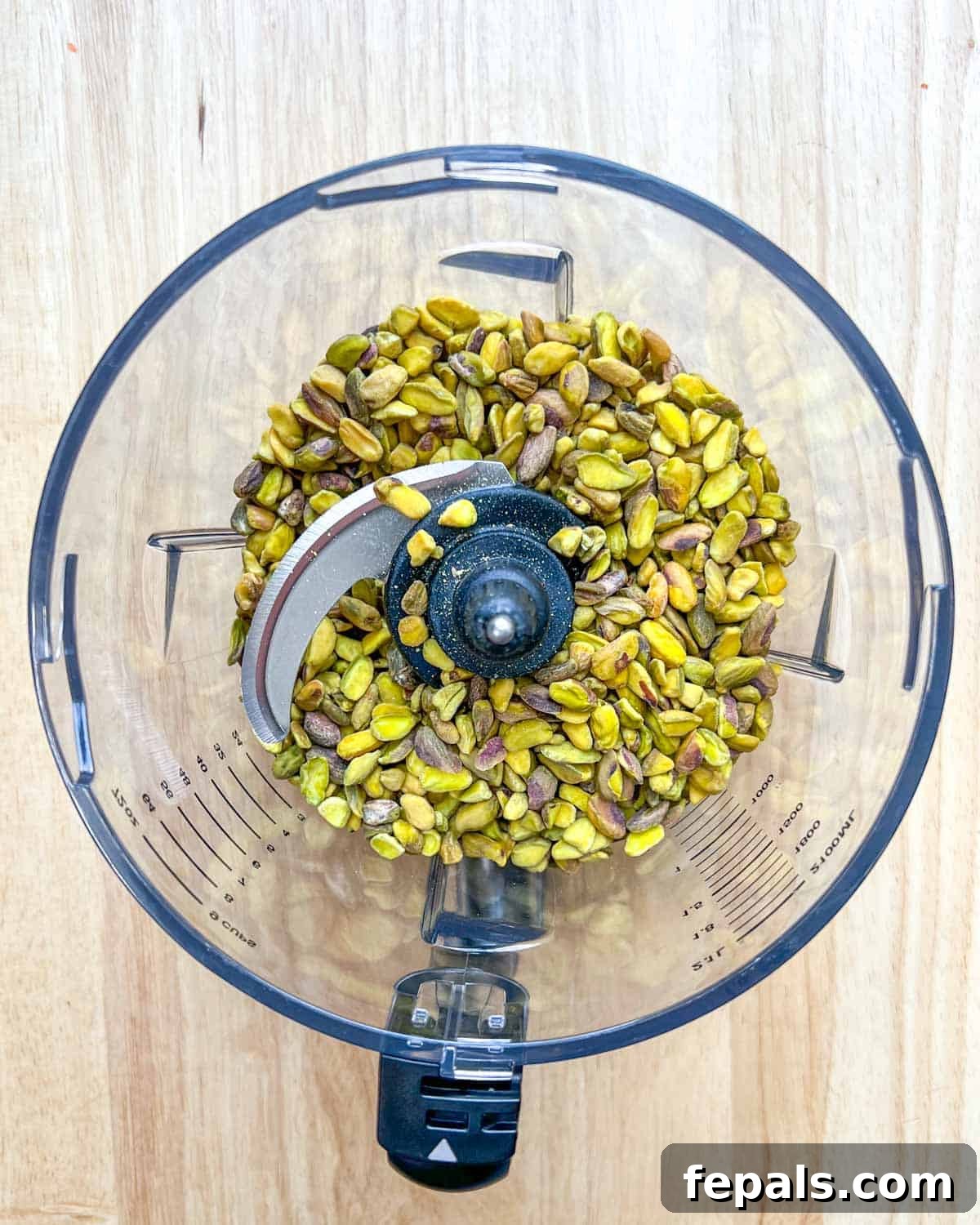 Decadent Pistachio Cream 4 Raw pistachios being added into the bowl of a high-powered blender, ready for processing.