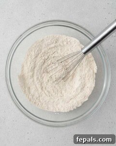 Power Banana Loaf 12 A bowl containing dry ingredients for protein banana bread, including flour, protein powder, baking powder, baking soda, cinnamon, and salt, all whisked together for even distribution.