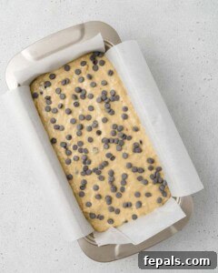 Power Banana Loaf 15 Protein banana bread batter poured into a parchment-lined loaf pan, with extra chocolate chips sprinkled on top for a delightful finish before baking.