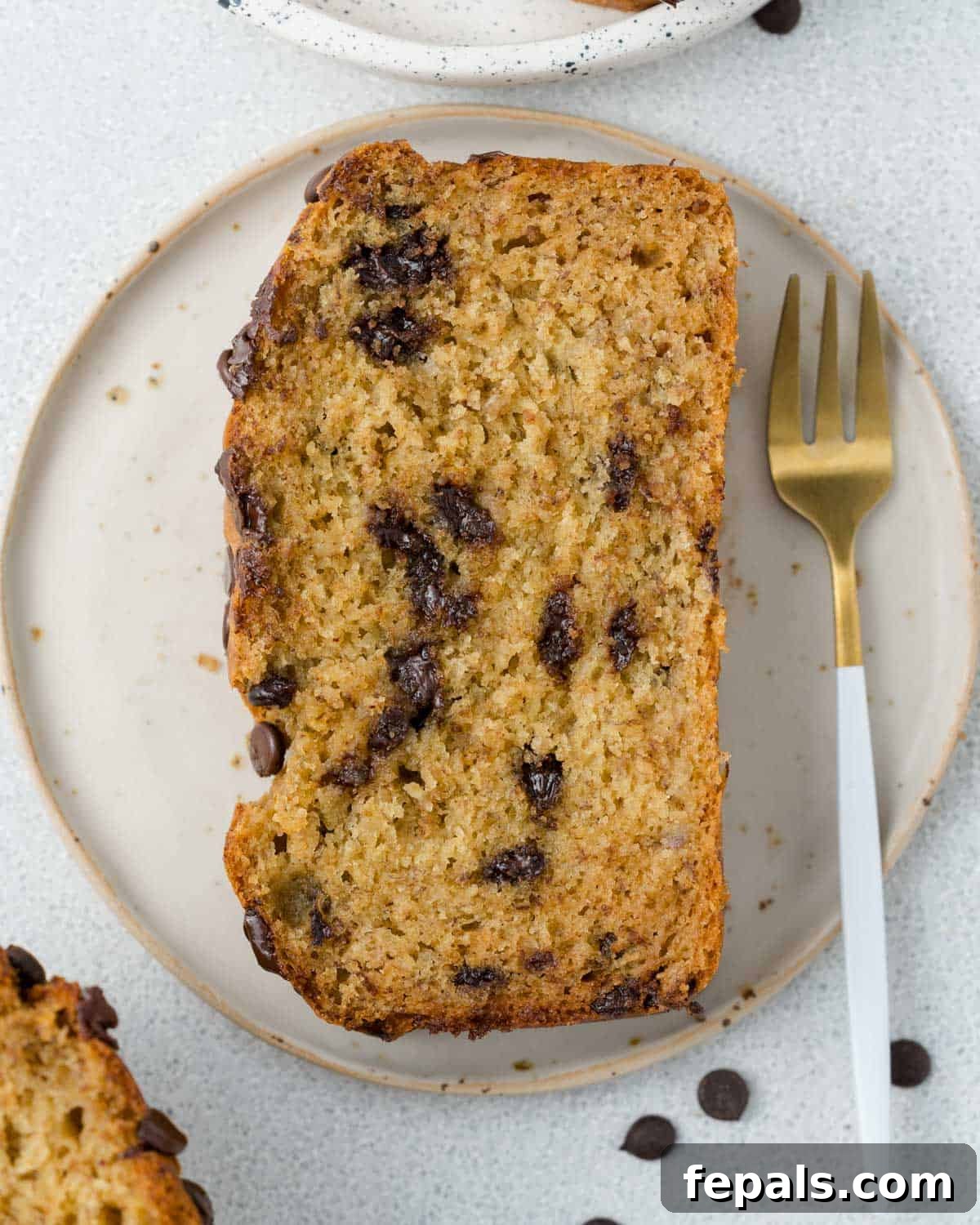 Power Banana Loaf 7 A perfectly sliced piece of protein banana bread, displaying its moist crumb, rich texture, and melty chocolate chips, resting elegantly on a pristine white plate with a fork beside it.